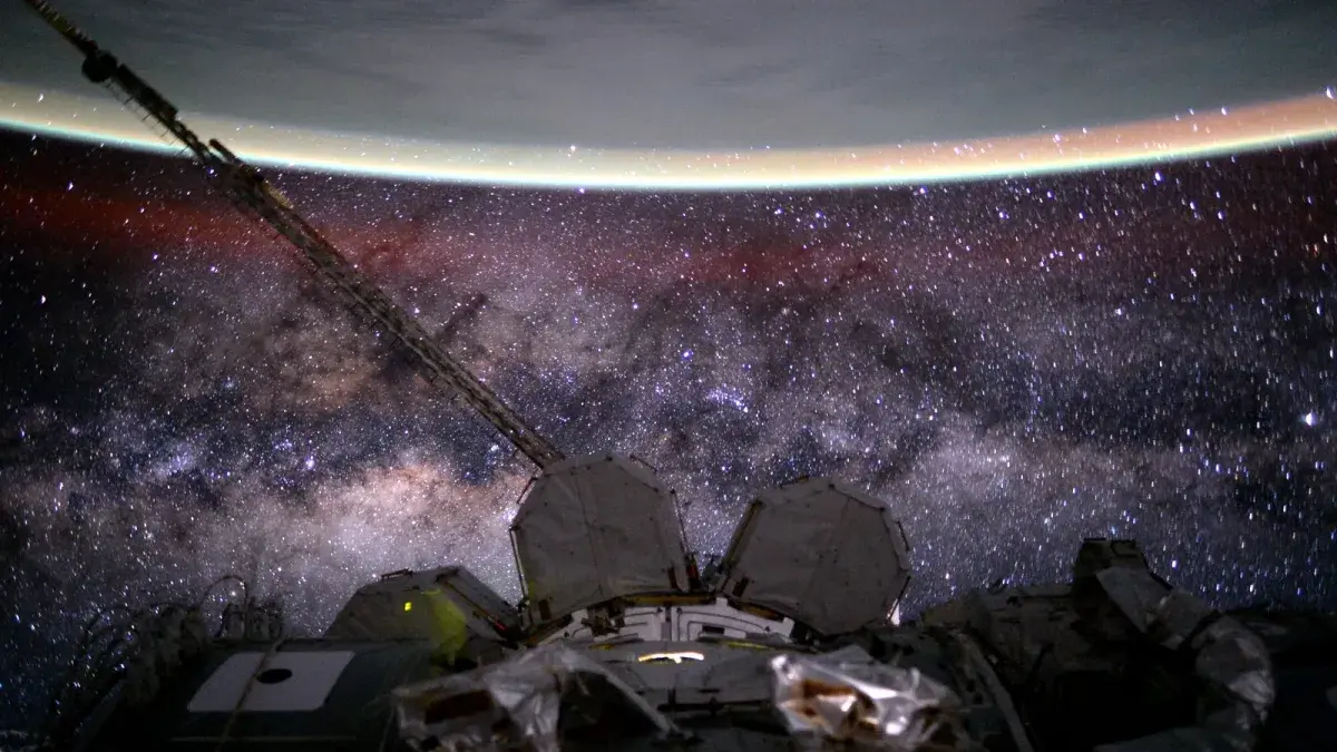 The Milky Way stretches below the curve of Earth's limb in the scene that also records a faint red, extended airglow.