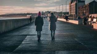 Two people walking along shoreline in a city