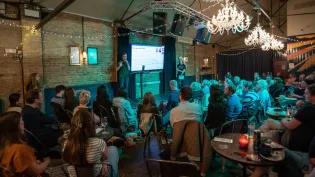 A speaker delivering a presentation a crowded pub.
