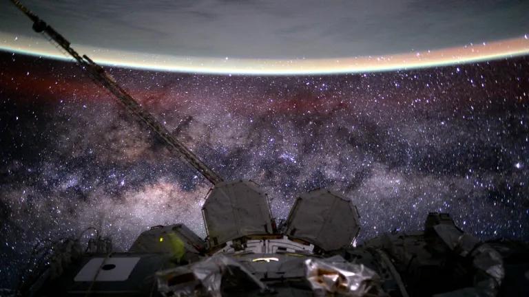 The Milky Way stretches below the curve of Earth's limb in the scene that also records a faint red, extended airglow.