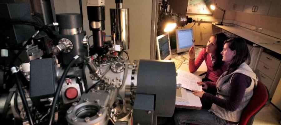 Two female scientists seated looking at computer monitors and surrounded by scientific equipment including Ion Micro-Probe