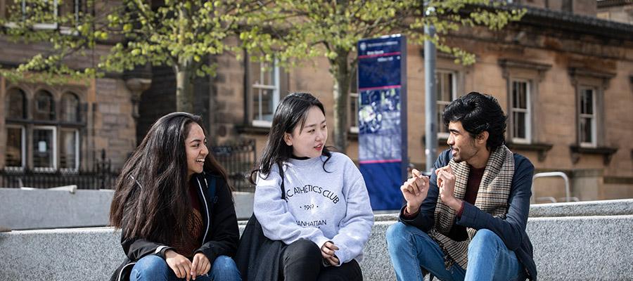 Three students chatting to each other, sitting outside on campus grounds.