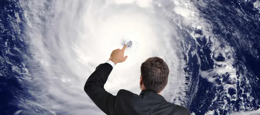 A man in a suit points at the eye of a hurricane on a screen