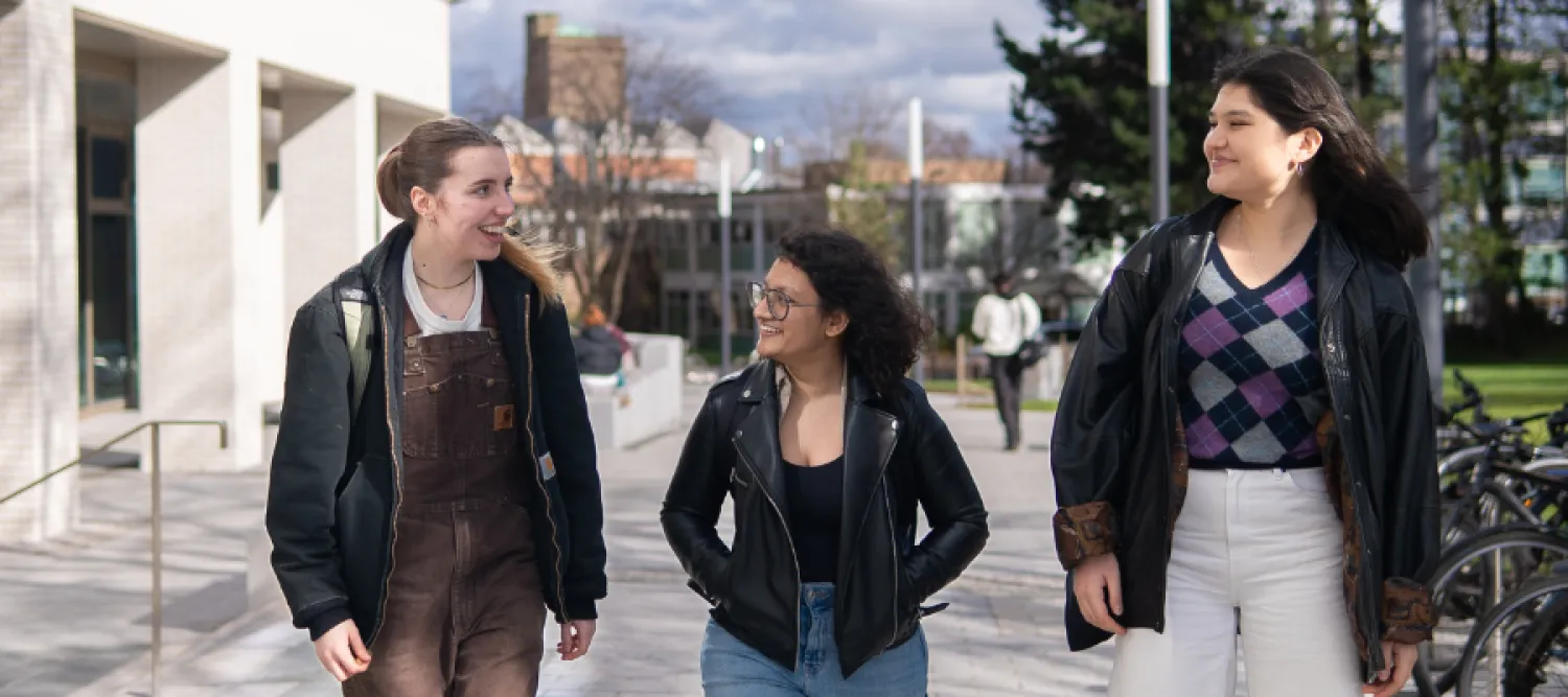 Three female students chatting to each other as they walk past the library.