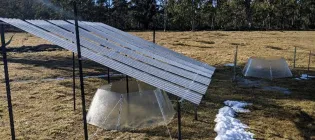 A rainout shelter with a warming chamber below it is placed in the middle of a field