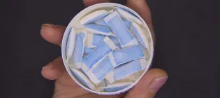 A container of nicotine pouches being held in a hand