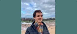 Rogelio smiling and looking into the distance. There is a beach in the background.