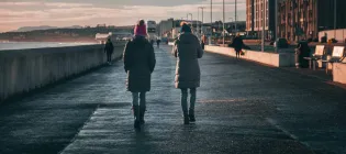 Two people walking along shoreline in a city