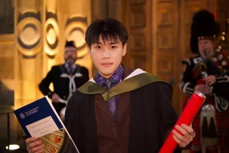 Rongsheng poses for the camera wearing his graduation robes and holding his certificate and scroll