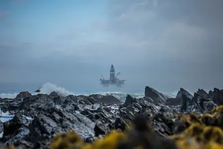 An oil rig entering Cape Town harbour on a misty morning in Sea Point, with rocks on the coastline in the foreground