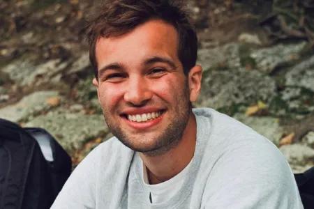 Luis in a grey shirt smiling into the camera with a rocky background.