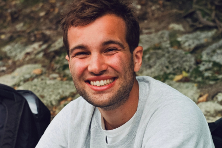 Luis in a grey shirt smiling into the camera with a rocky background.