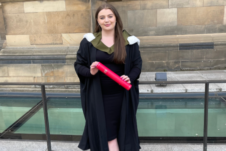 Erin wearing a black robe and holding her degree at graduation.