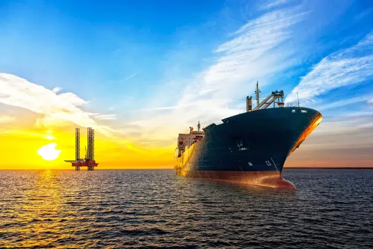 A ship and an oil rig in the ocean at sunset