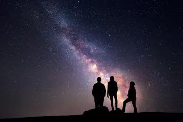 Three people standing together gaze at a galaxy and stars in the night sky