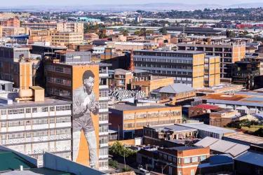 A picture of a cityscape on a sunny day full of apartment buildings. One of them has a mural of a man on it