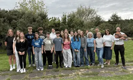 Some students pose for a group photo, and one member of the group is holding a musical instrument
