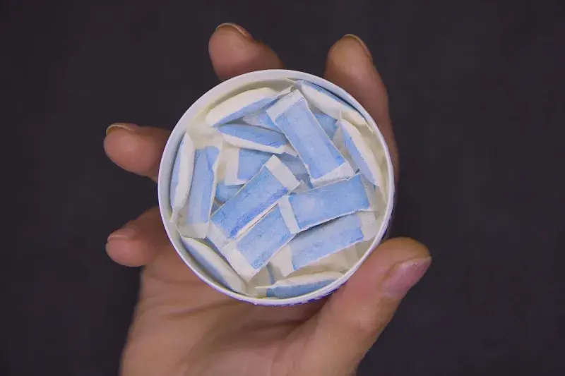 A container of nicotine pouches being held in a hand