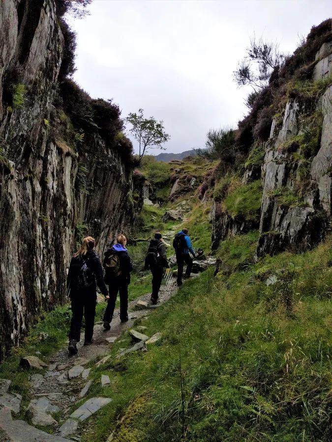 A group of people are seen walking on a path surrounded by high rock walls.