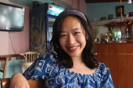 Siying smiling for a photo while sitting in a cafe.