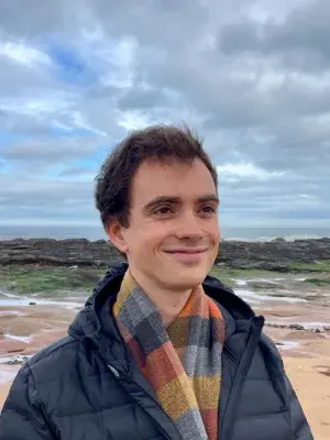 Rogelio smiling and looking into the distance. There is a beach in the background.