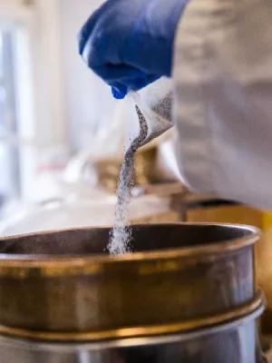 Surgical gloved hands pouring rock sediment into a large sieve 