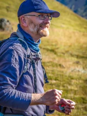 A male academic wearing a hat and weather gear smiling as he stands and teaches on a hillside in Iceland