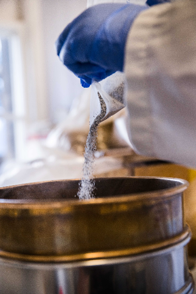 Surgical gloved hands pouring rock sediment into a large sieve 