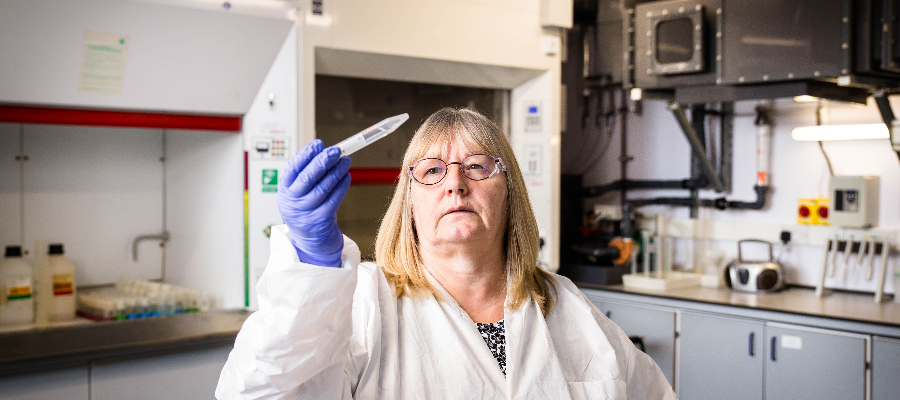 Female scientist wearing lab coat and gloves holding up a dropper in an aluminium beryllium laboratory