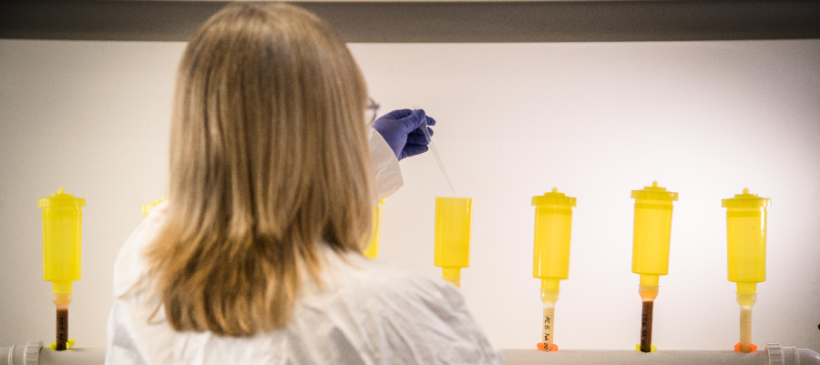 A female scientist wearing lab coat and gloves dripping chemicals into a column of analysis receptacles for anion analysis