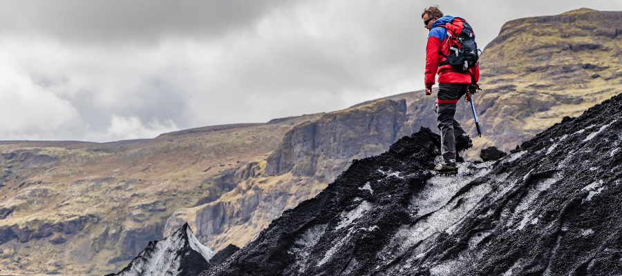 A male researcher in ice climbing gear standing on a mountain cliffside in the Icelandic landscape