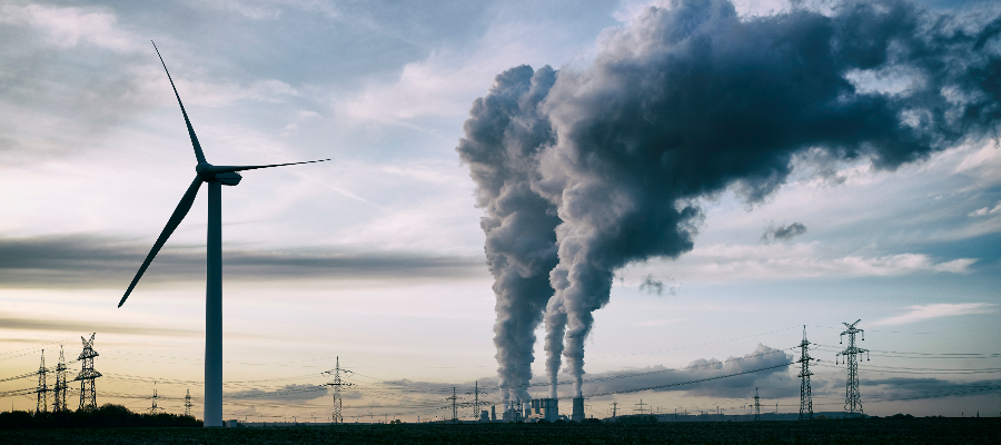 Single wind turbine, and a coal burning power plant with pollution and electricity pylons in the background