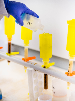 A close view of blue gloved hands dropping chemicals into yellow scientific receptacles for anion analysis