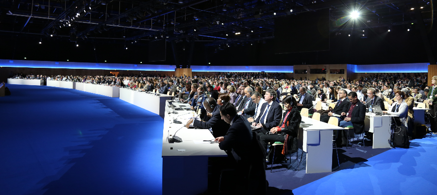 A large conference room filled with hundreds of seated delegates at the 2015 UN Paris Climate Change Conference