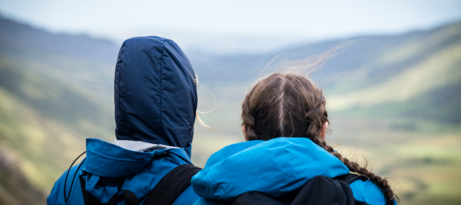 A photo taken from behind two university students in hiking gear as they look down into a valley landscape in Wales