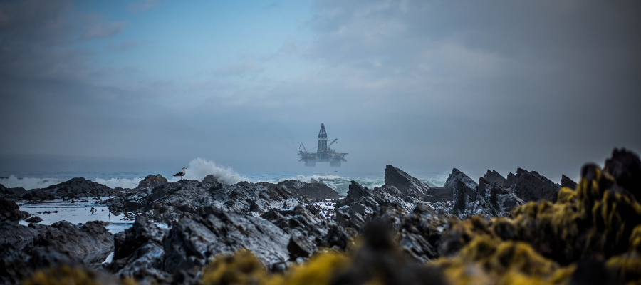 An oil rig entering Cape Town harbour on a misty morning in Sea Point, with rocks on the coastline in the foreground