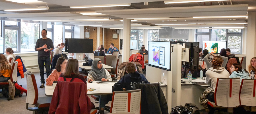 A room with university students seated at desks with a large computer at the end of each, in the GIS computing suite