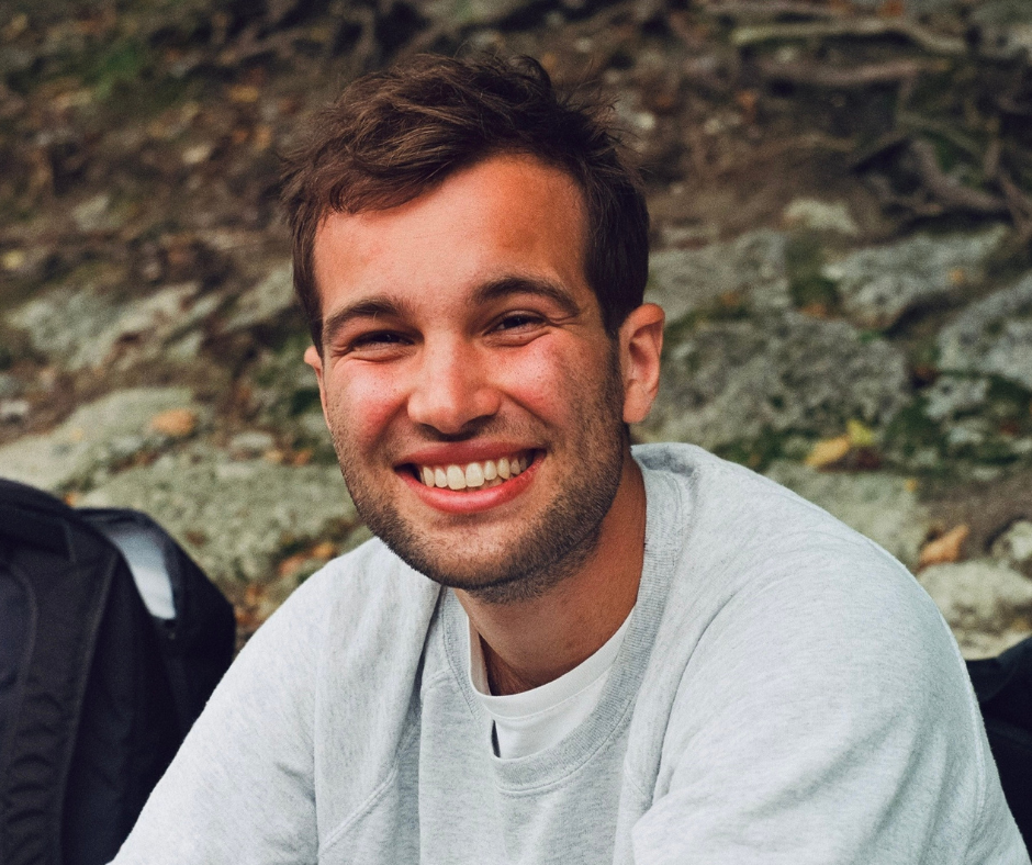 Luis in a grey shirt smiling into the camera with a rocky background.