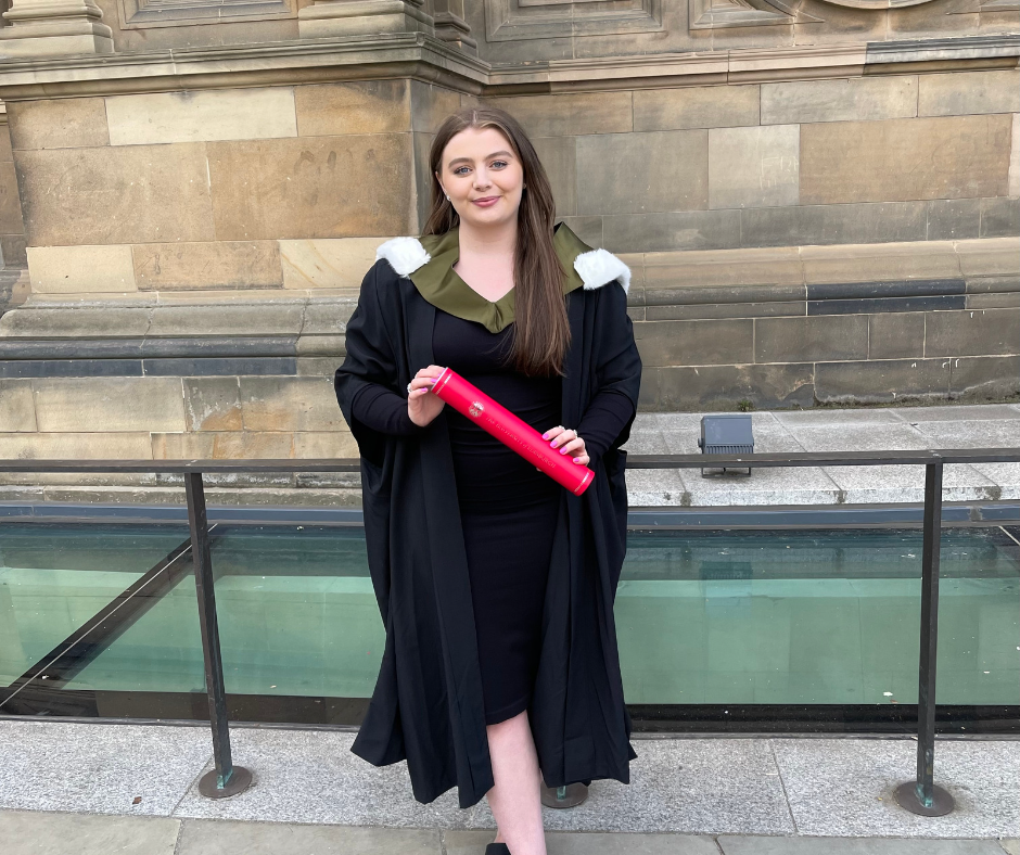 Erin wearing a black robe and holding her degree at graduation.