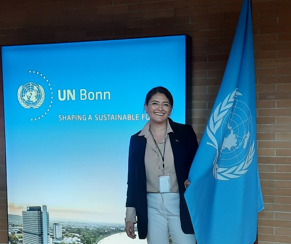 Valentina DaCosta standing beside a UN flag at a UN conference.